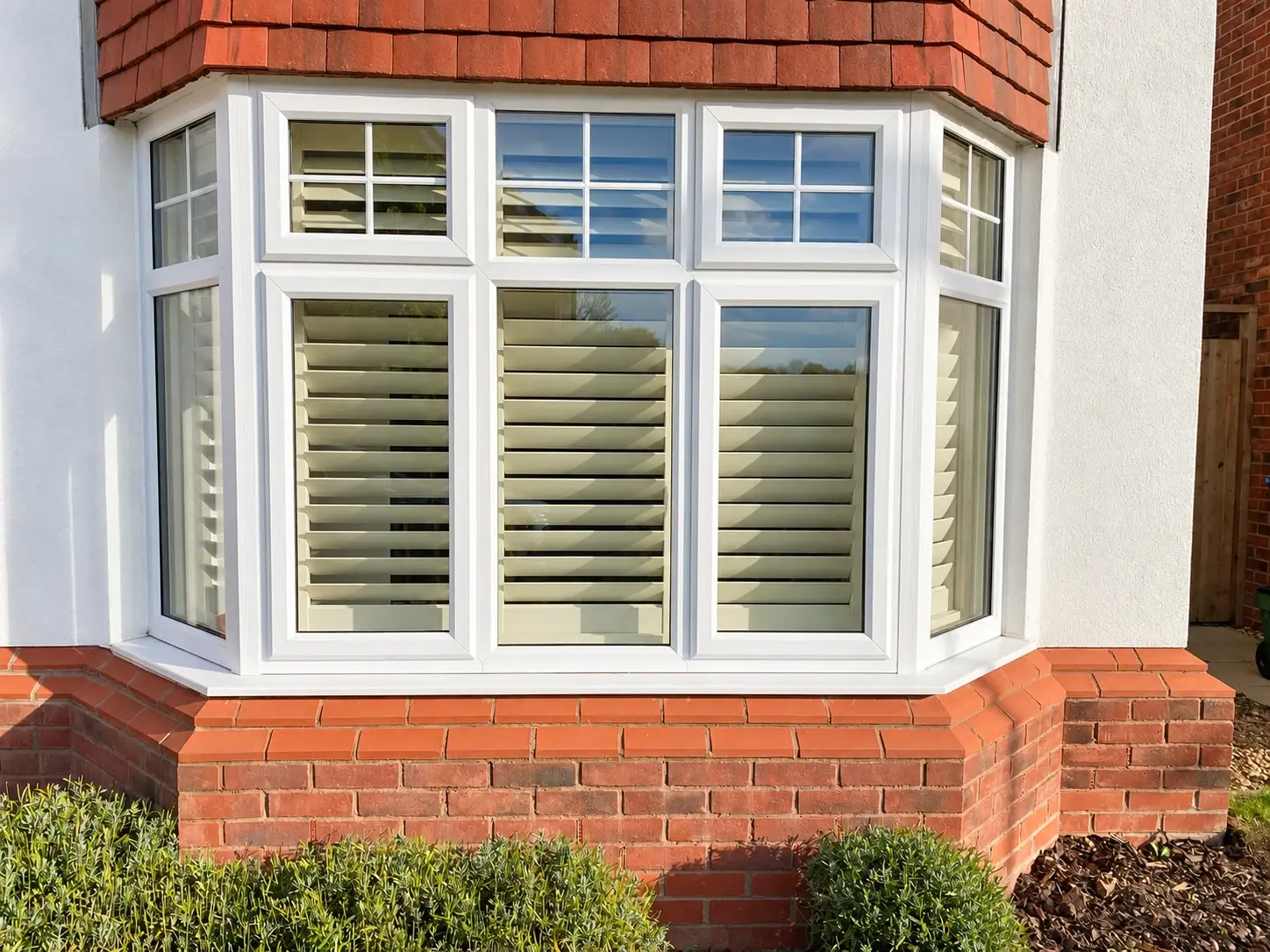 Ivory wooden shutters seen through the ground-floor bay window from outside the Hinckley home