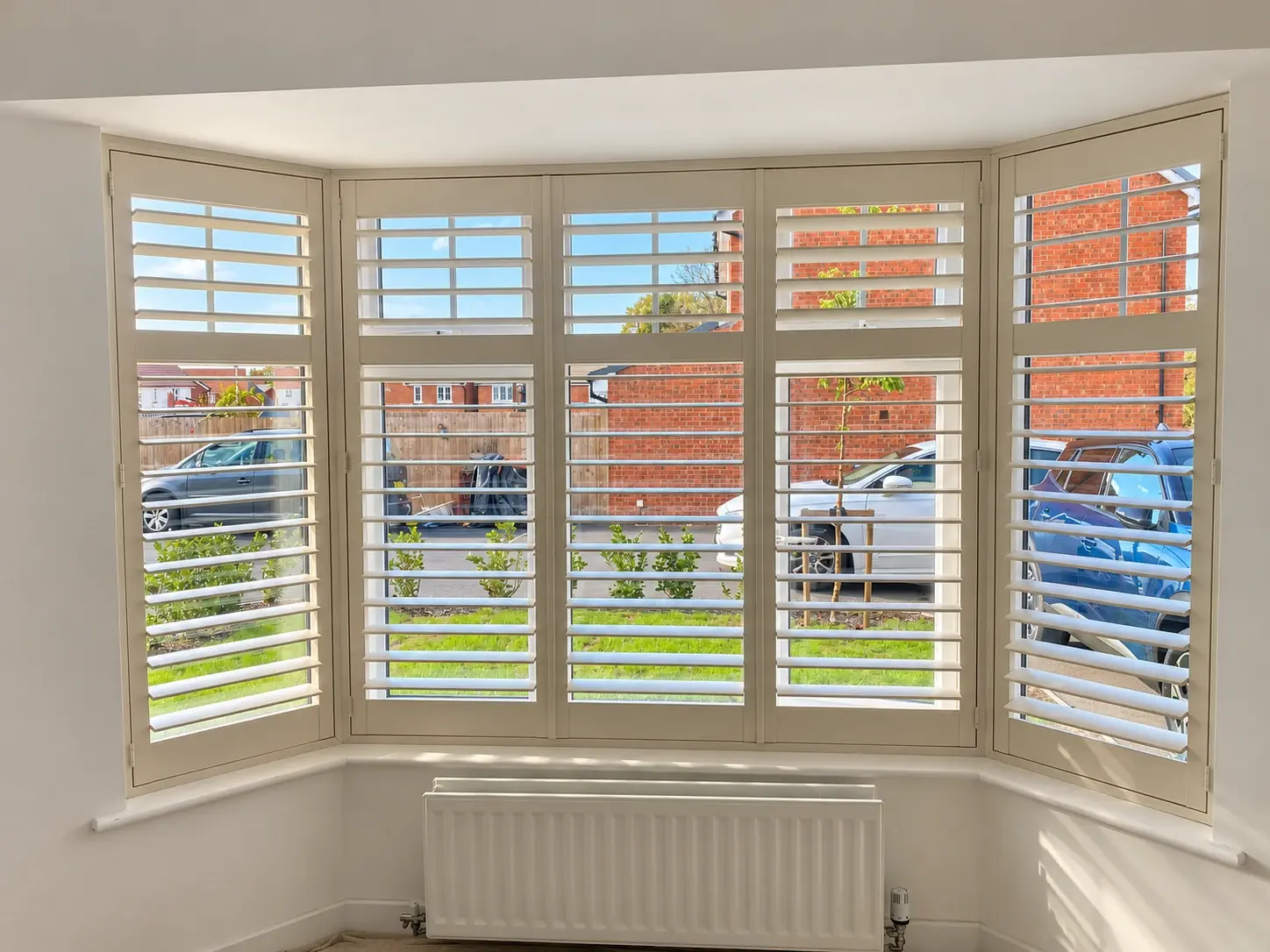 Ivory full-height Paulownia shutters with midrails and open 89 mm louvres across a living-room bay window in Hinckley