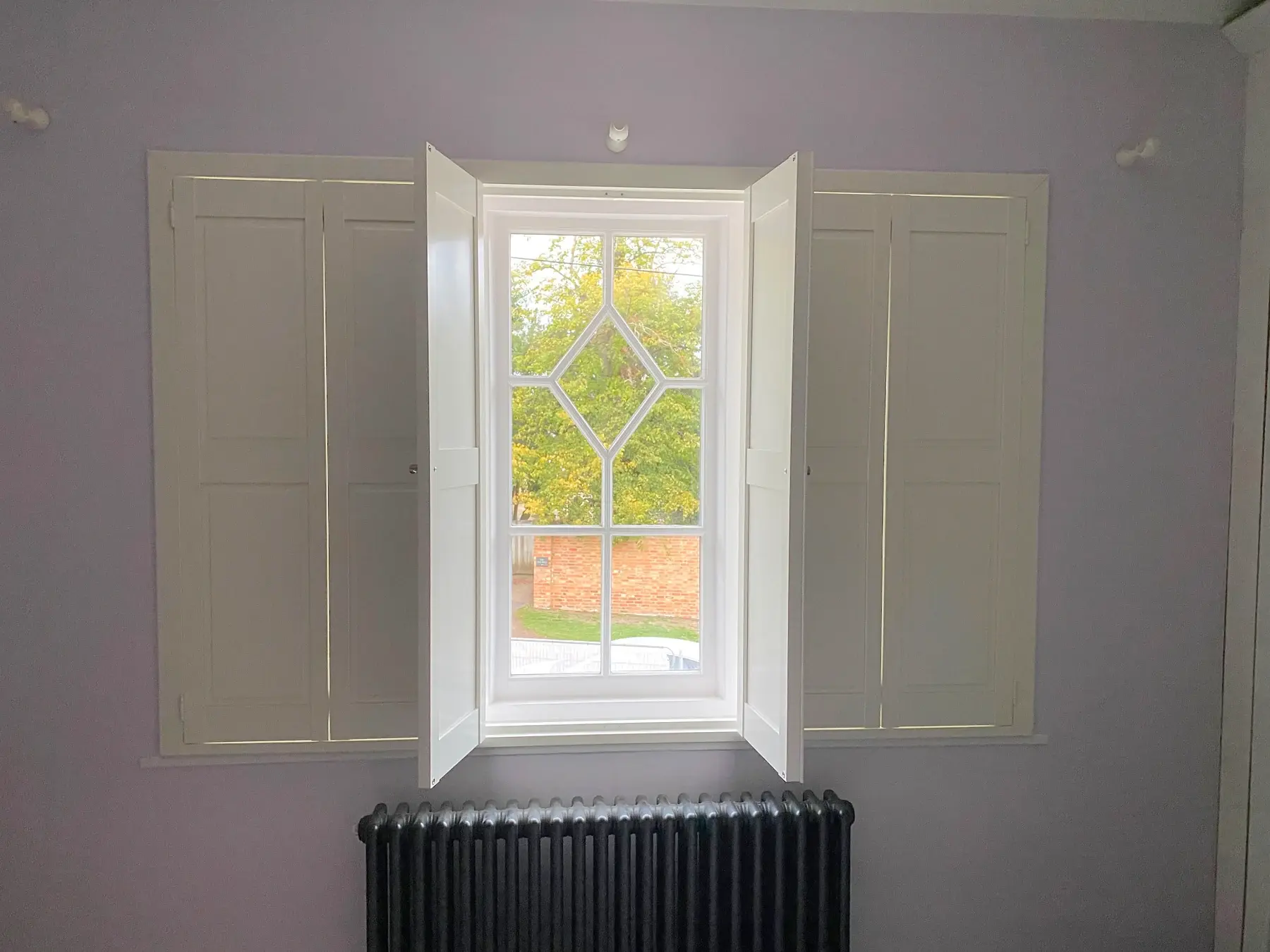 Silk White solid panel shutters with centre panels open around decorative glazing