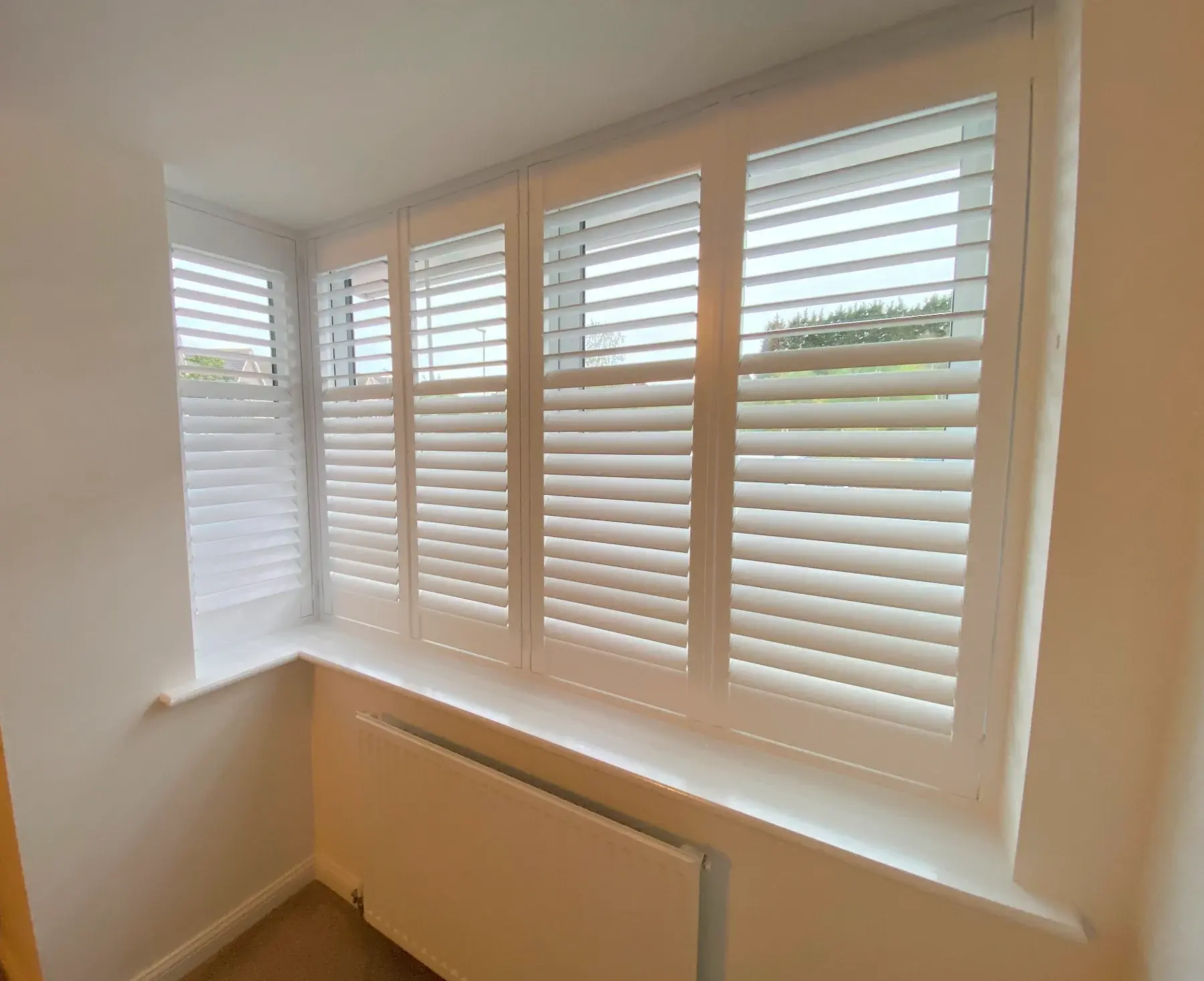 Full-height shutters with 63 mm louvres in Wellingborough: The bay window viewed from inside, with different upper and lower louvre settings.