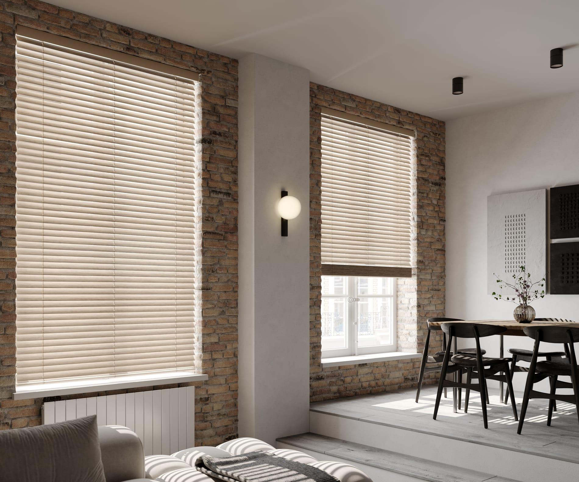 Beige smooth-finish faux wood venetian blinds across tall windows in an exposed-brick living and dining space