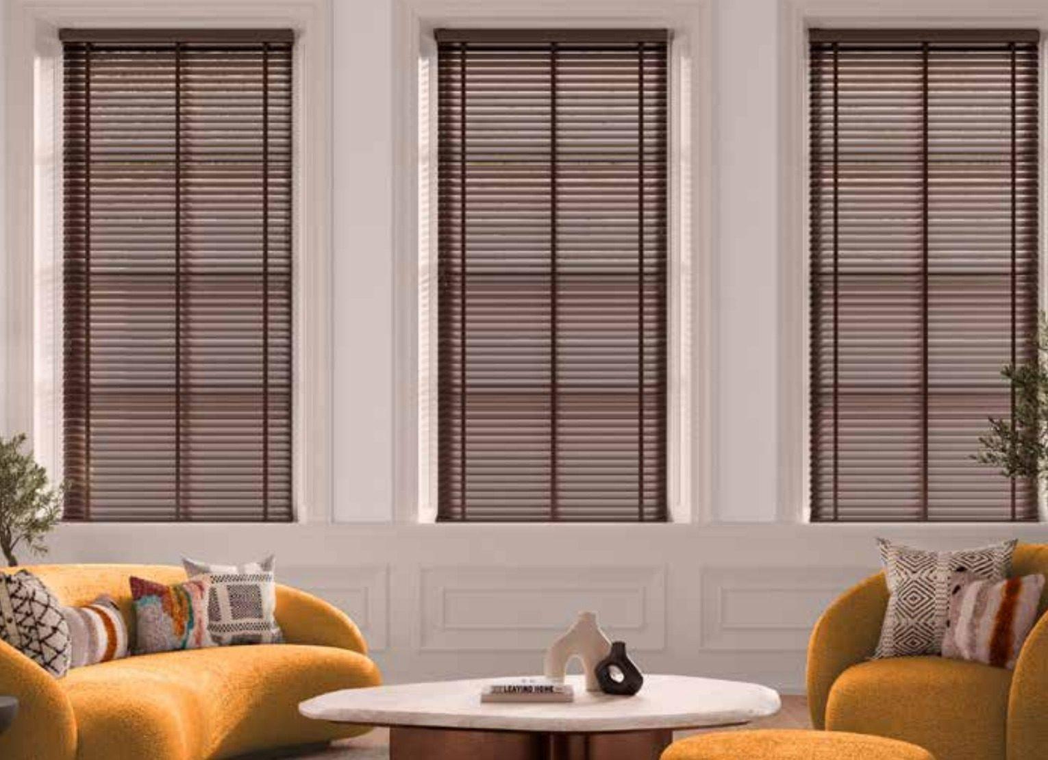 Dark bronze wide-slat aluminium venetian blinds across three windows in a living room
