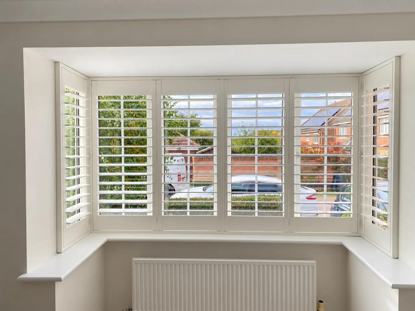 Full-height Paulownia wood shutters in Silk White with open 89 mm louvres across a box bay window in Market Harborough